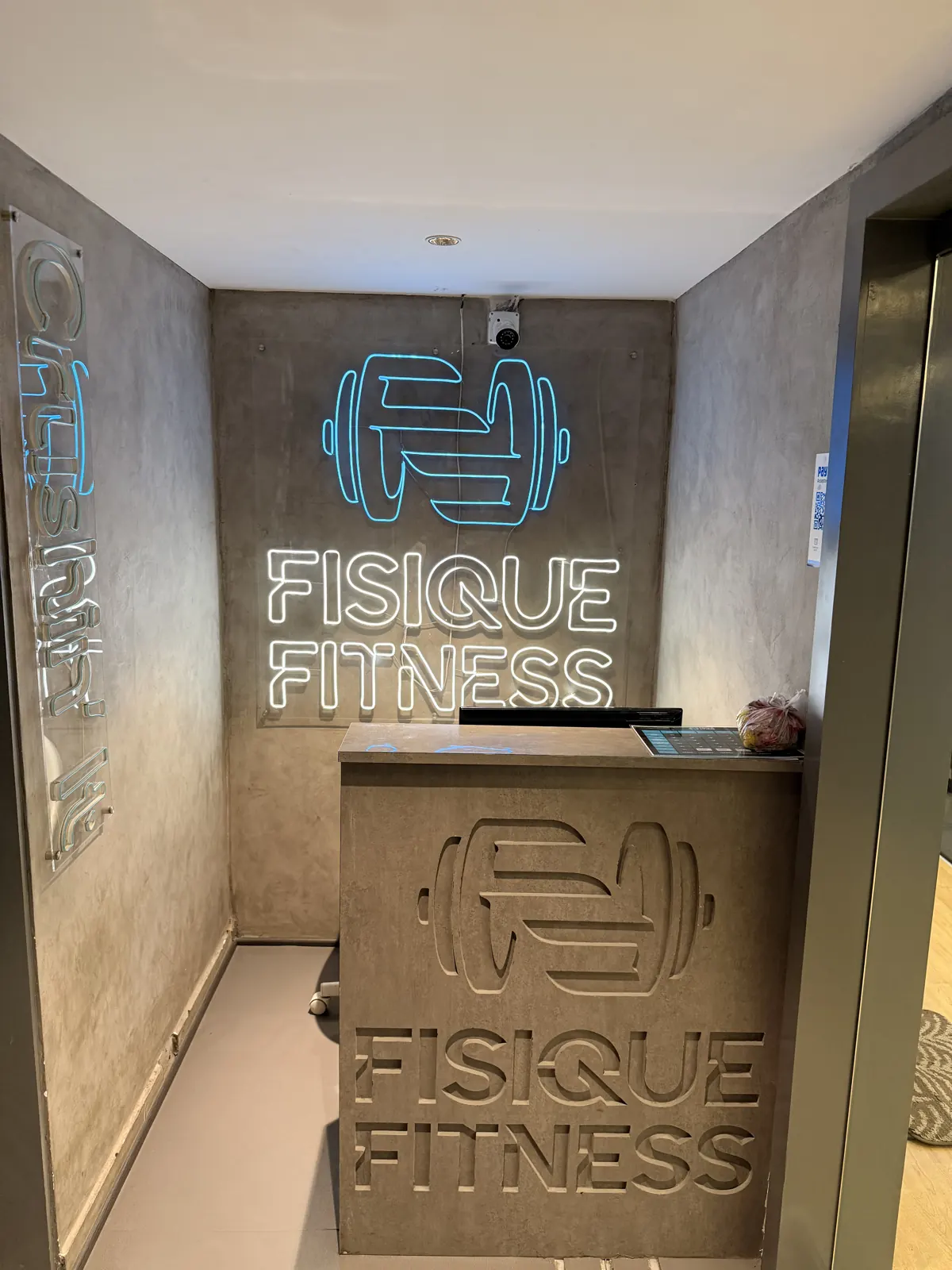 The Fisique reception with the neon logo on a concrete wall